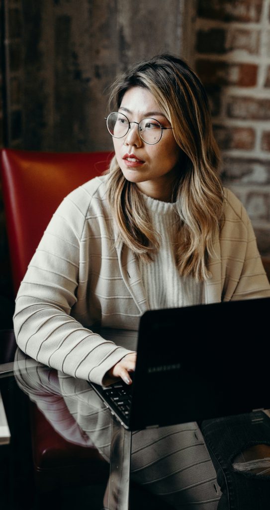 Frau Mitte 30 aus Ostasien sitzt nachdenklich und schaut zur Seite, während sie online nach Karrieremöglichkeiten in Deutschland sucht.