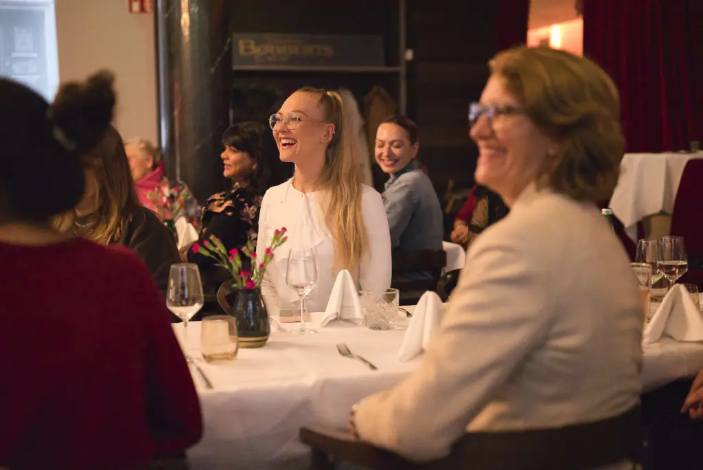 Frauen lachen und unterhalten sich während eines HerCentury-Netzwerktreffens in gemütlicher Atmosphäre.